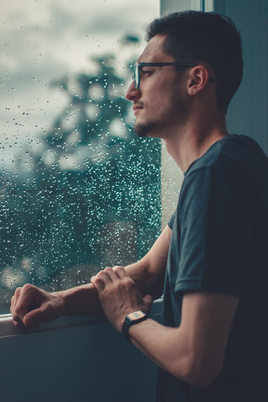 man leaning on glass window watching the rain